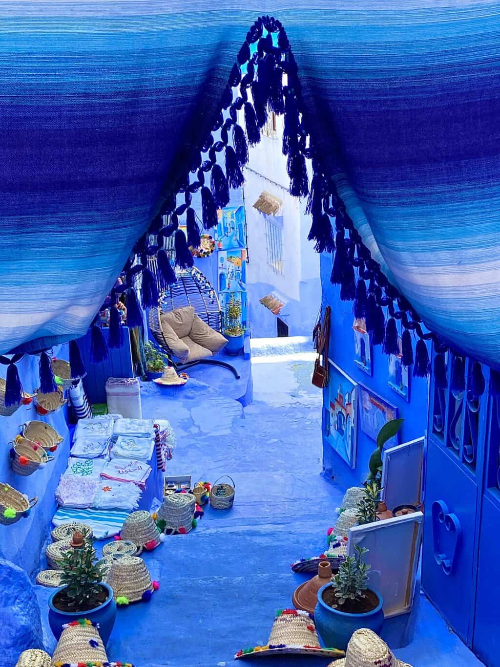 Chefchaouen street with blue sidewalk, a blue curtain, and items for sale on the steps