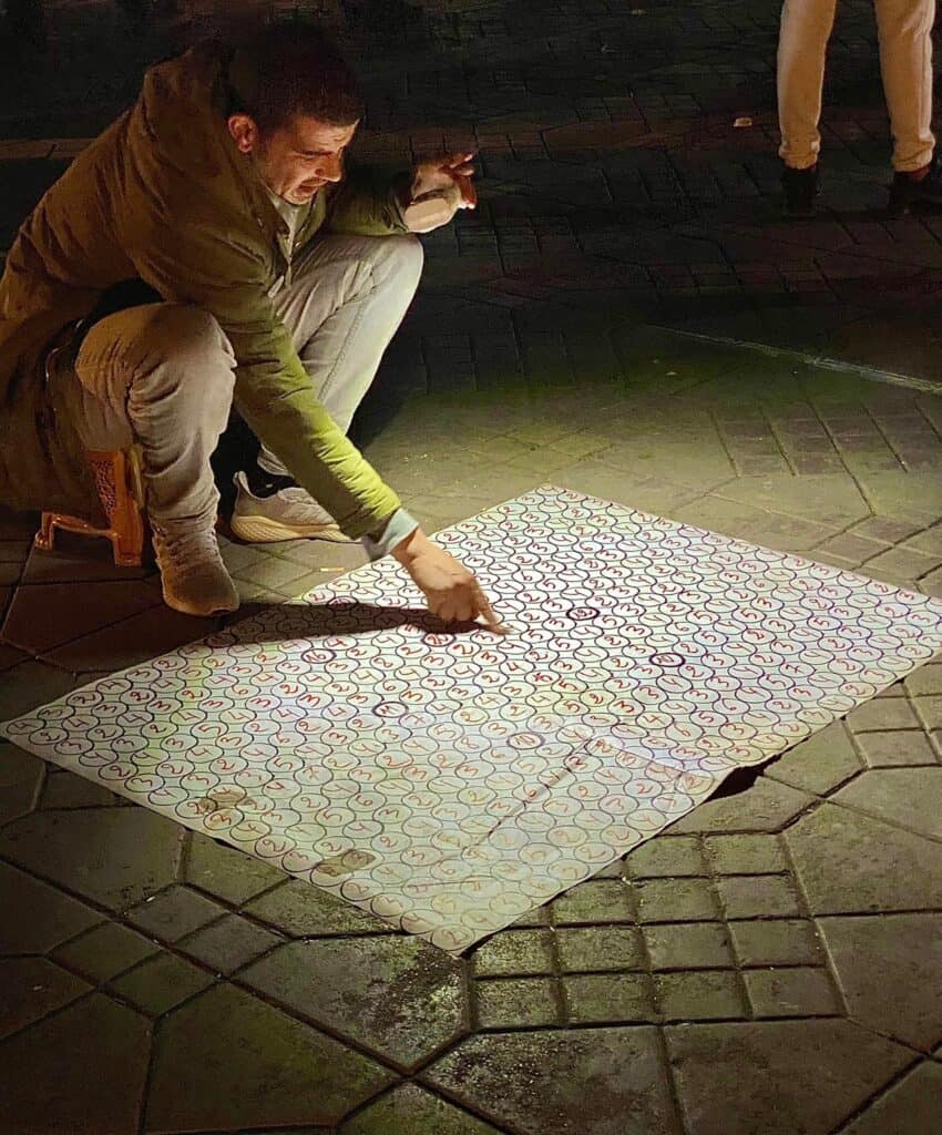 Man pointing at a numbers game of chance at night in Jemma El Fnaa square in Marrakech Morocco