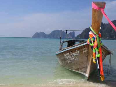 Thailand long boat with colourful ribbons on the bow and Thai writing on the side on clear blue water with rocks in the background