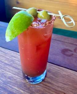 Ceasar cocktail made of clamato juice with green olives on a stick and a lime