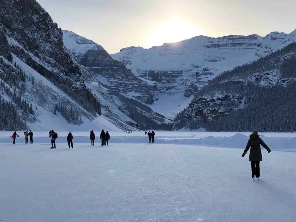 Winter in Lake Louise with snow covered mountains and people skating on an ice rink in the foreground