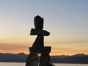 Inukshuk Inuit stone structure in front of ocean with sun setting in the background over mountain ranges