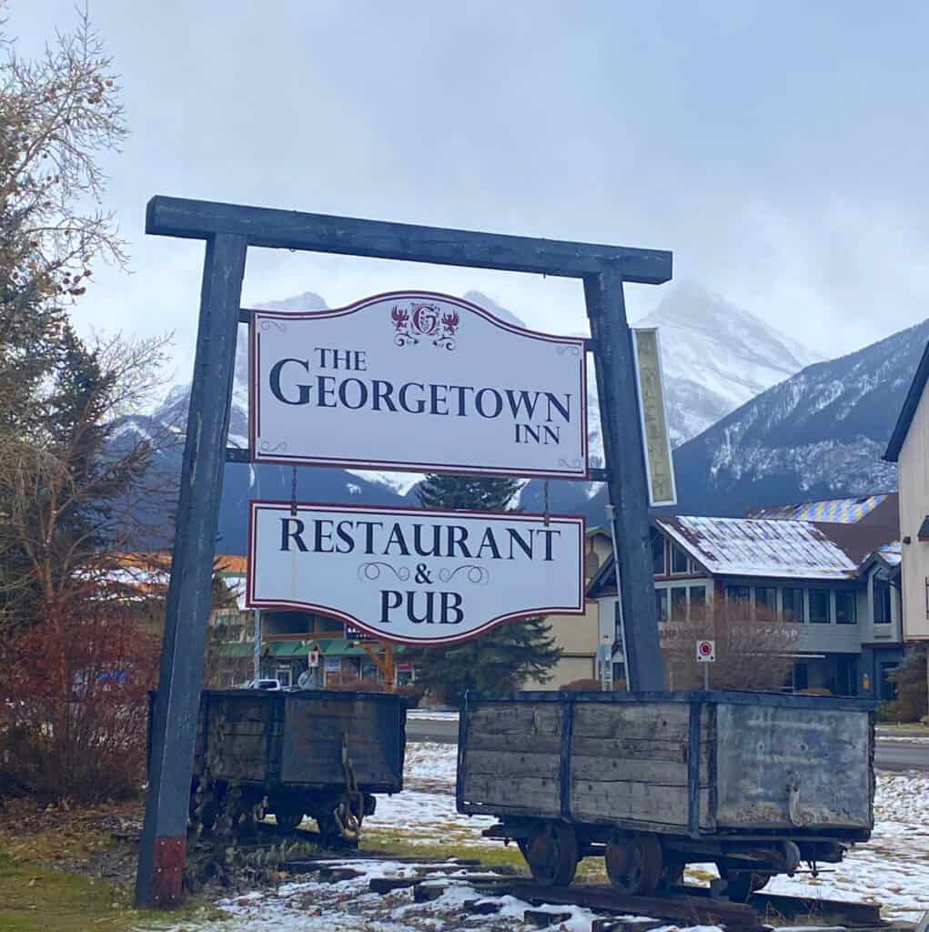 Sign that says Georgtown Inn Restaurant and Pub with mountains in background and 2 wooden carts below sign