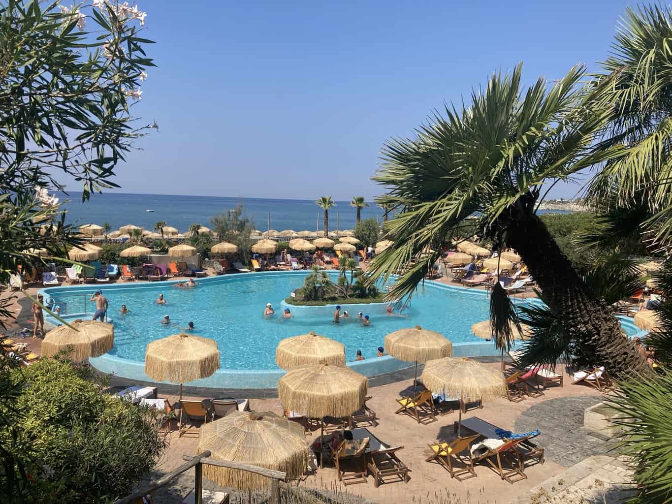 People swimming in Poseidon Thermal Gardens hot pool in Ischia Italy with lounger chairs and umbrellas above
