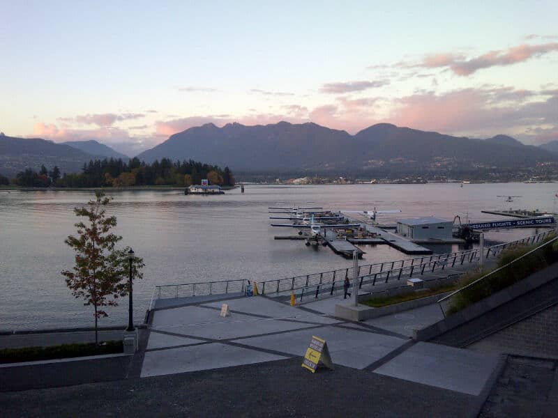 Vancouver British Columbia Coal Harbour with ocean, a dock, float planes, and mountains in the background as the sun is setting