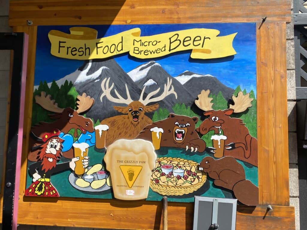 Grizzly Paw Brewery wooden sign picturing wild cartoon animals drinking beer and eating in front mountains
