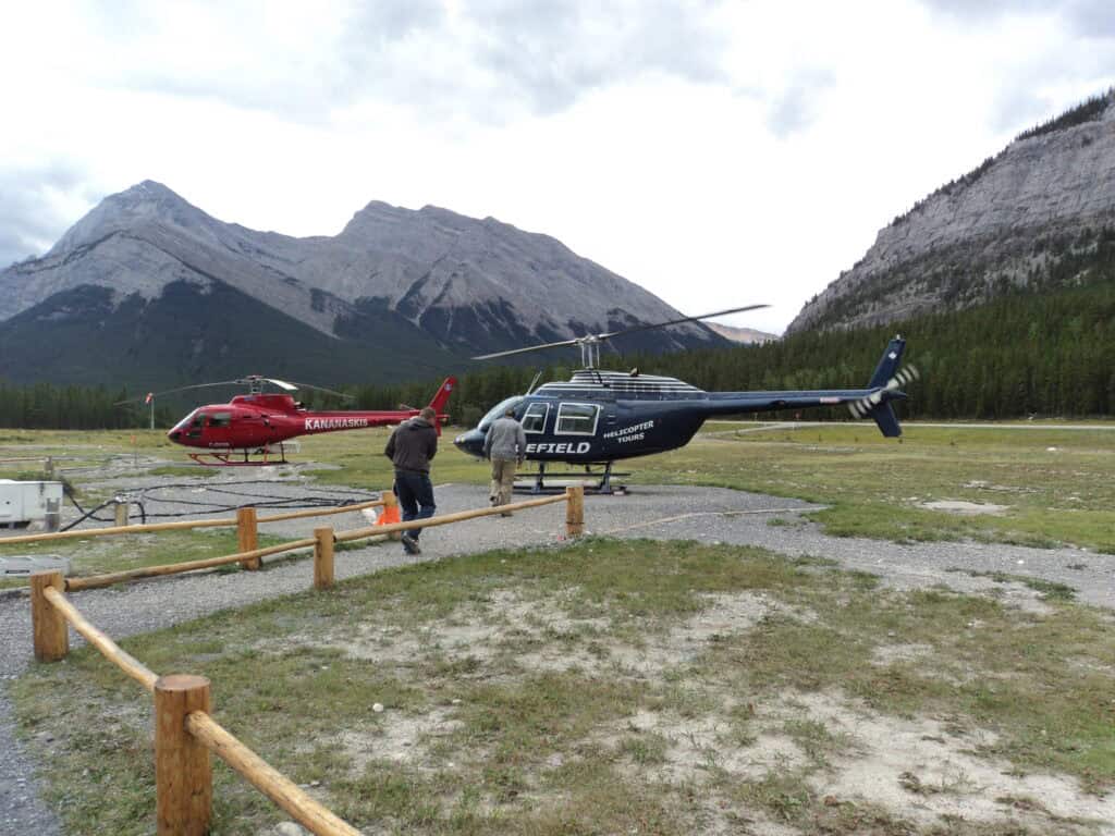 Two helicoptors on landing pad with mountains in the background